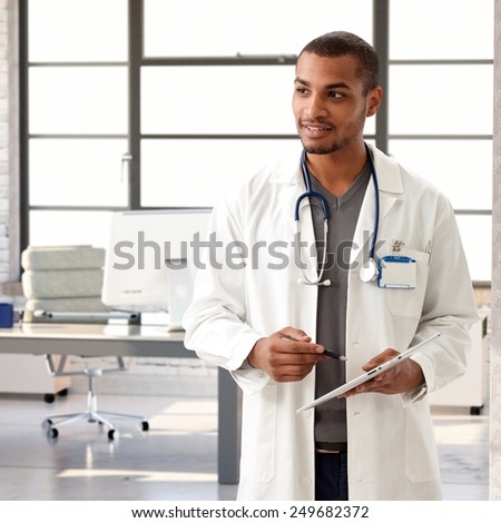Young black male doctor holding tablet, looking away.