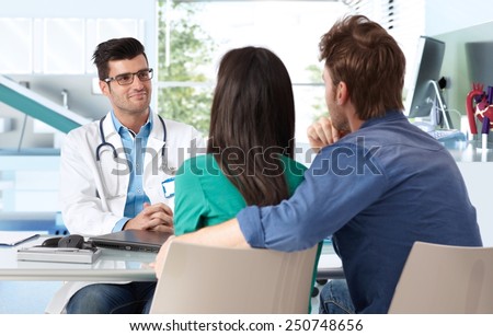 Male doctor consulting with young couple in doctor\'s room.