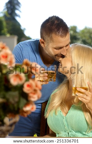 Portrait of romantic young couple kissing with drinks in hand, outdoors. Attractive, busty blonde woman with cleavage.