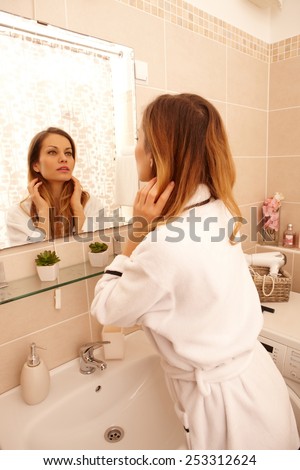 Young woman watching her face in mirror in the morning in dressing gown.