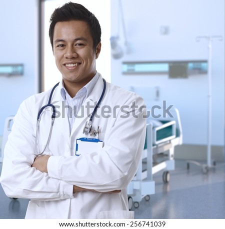 Portrait of happy asian doctor in lab coat standing at hospital room, smiling.