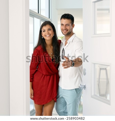 Happy young attractive caucasian couple standing in new home doorway. Smiling, standing, gesturing, home finance.