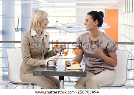 Mid-adult casual caucasian businesswomen talking about business at trendy cafe, sitting at table, having fun.