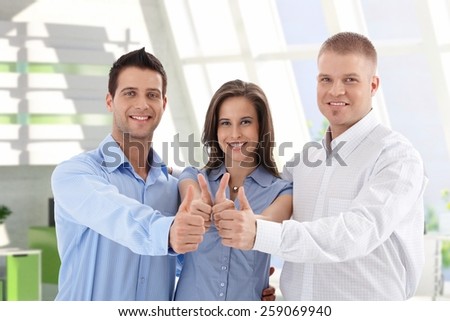 Successful young caucasian casual startup business team giving thumbs up at financial center. Smiling, standing, looking at camera.