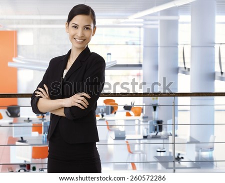 Attractive, happy, asian businesswoman at high-tech business office with arms crossed. Smiling, arms crossed, standing upstairs. Copyspace.