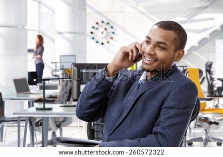 Happy, smiling, successful afro american business advisor talking on mobile phone while sitting at office table, Bright, suit no tie.