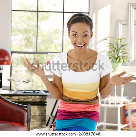Young afro-american woman laughing happy with arms wide open, looking at camera at home.