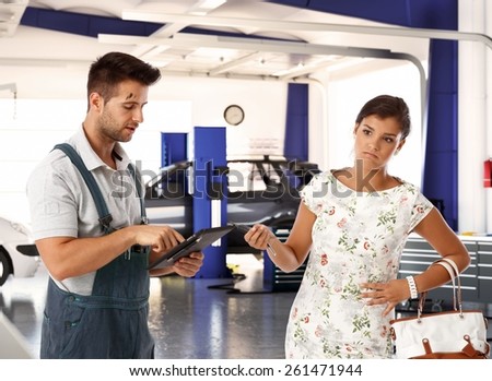 Elegant young woman with disgust on face handing car key to car mechanic.