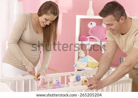 Pregnant mother and husband preparing baby's cot, smiling.