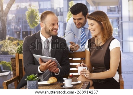 Happy caucasian business team having an outdoor meeting at restaurant using tablet computer.