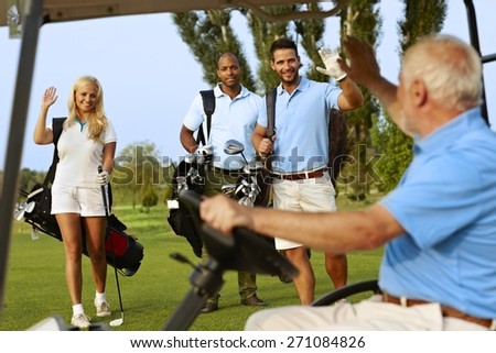 Golfers greeting on golf course, waving, smiling.
