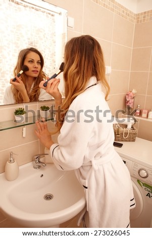 Attractive young woman putting on makeup in the morning using mirror.