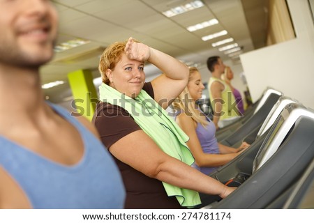 Exhausted fat woman training on running machine in gym.