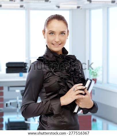 Portrait of elegant young female secretary at executive office, smiling.