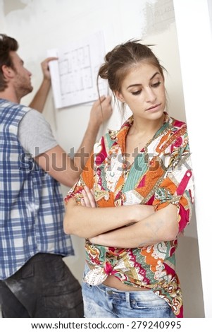 Young couple planning new home, woman sulking, man looking at floor plan.