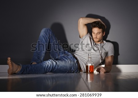 Depressed young man lying on floor, drinking alone.