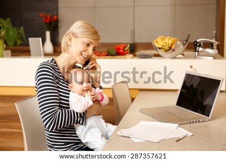 Young mother working from home, holding baby on lap.
