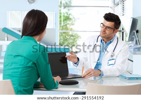 Doctor consulting with patient in doctor\'s room, presenting results on laptop computer.
