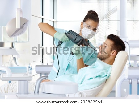 Aggressive female dentist using power drill for drilling patient\'s tooth.