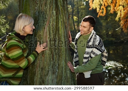 Happy casual caucasian couple playing catch me around tree outdoor at autumn forest. Having fun, hiking, smiling.
