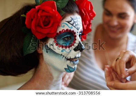 Makeup artists in work making a Halloween makeup - mexican Santa Muerte mask.