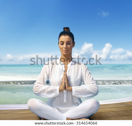 Young woman relaxing on the beach in prayer position, sitting eyes closed.