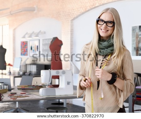 Portrait of happy casual trendy caucasian blonde fashion designer businesswoman at studio. Smiling, standing, looking at camera.