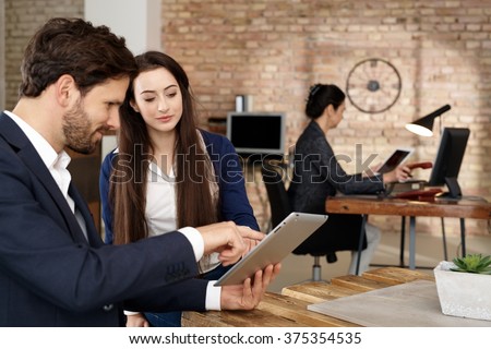 Businesspeople using tablet computer, talking in office.