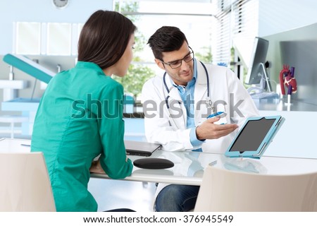 Doctor consulting with female patient, presenting results on tablet computer, sitting at desk.