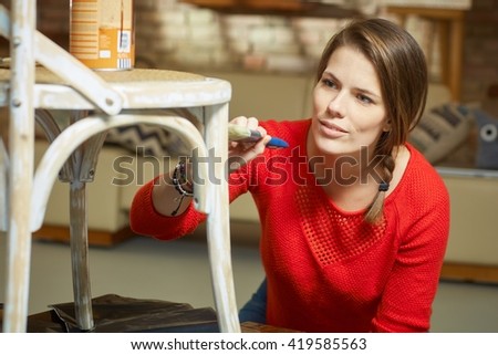 Attractive woman renewing, painting chair at home.