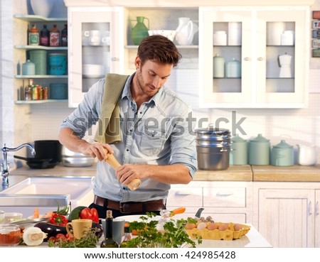 Young man preparing food at home in kitchen using pepper-mill.