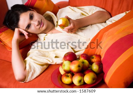Young women is resting on the couch and eating an apple.