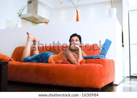 Young women is resting on the couch and surfing the internet on her laptop computer.  Maybe she is dreaming of an online friend.