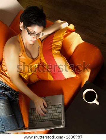 Young women is resting on the couch and surfing the internet on her laptop computer.
