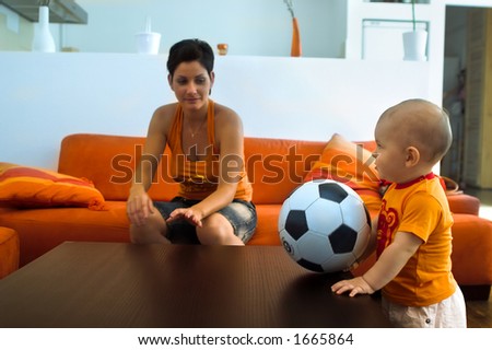 Baby is playing with a real soccer ball indoor.