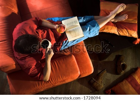 Man is lying on the couch and reading a book.