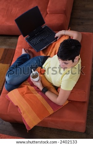 Young woman is sitting and resting on the sofa and taking a cafe break. Maybe she is surfing the net, chatting or studying for the next university exam.