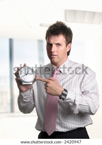 Conceptual image about the importance of time in the business. Businessman shows the time on a clock and he looks a bit angry.