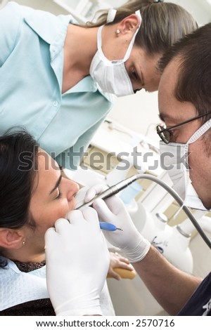 Dentist and his assistant are drilling the patietns tooth.