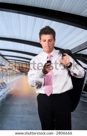 Businessman walks on a modern corridor and he is playing or dialing on his mobile phone.