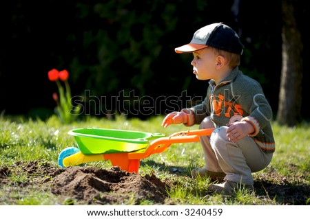 2 years old boy plays with toy tools in the garden.