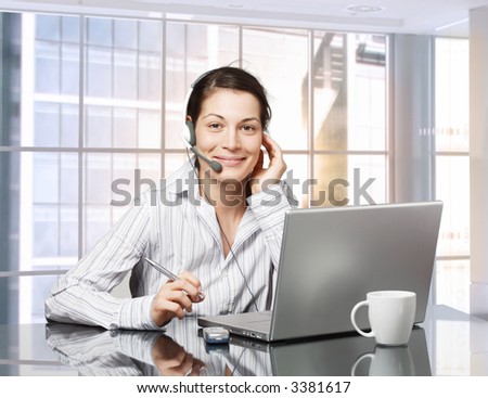 Young female receptionist works on laptop computer in brightly lit office. Daylight, indoor, office.