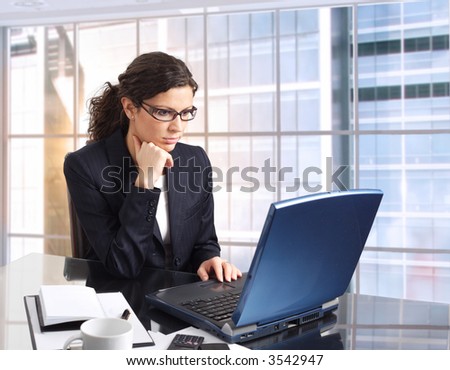 Young female office worker sits in front of her computer screen. Daylight, indoor, office. Dark cloth.