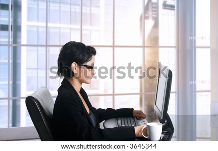 Young female office worker sits in front of her computer screen. Daylight, indoor, office.
