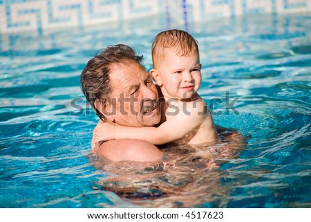 Grandfather and grandson swimming together in the pool. Outdoor, summer.