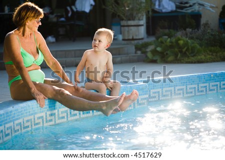 Grandmother and two years old grandson enjoy water and sunshine on the poolside. Natural light, summer.
