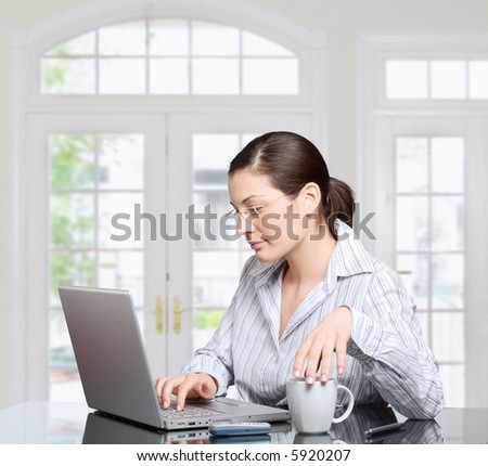 Young woman works on laptop computer. There is morning at home in a light and clean living room dominated by white and soft tones.