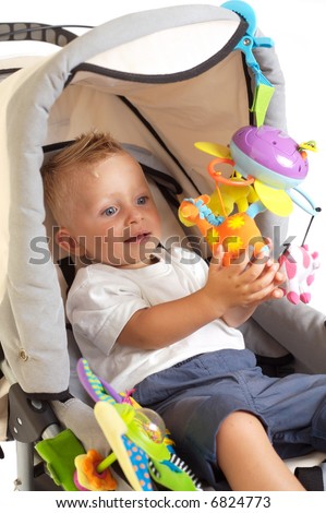 One year old baby boy is sitting in a stroller, smiling and playing with toys. All toys visible on the photo are officially property released.