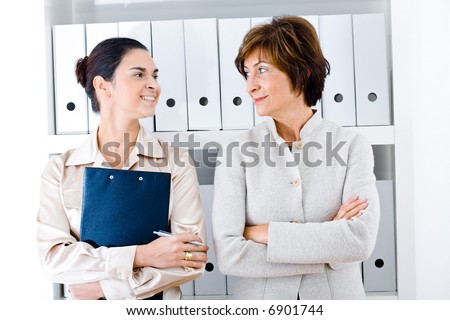 Portrait of a senior businesswoman with assistant in office, side by side, face to face, smiling.