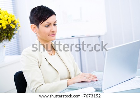 Businesswoman working on laptop computer in brightly lit office, smiling.
